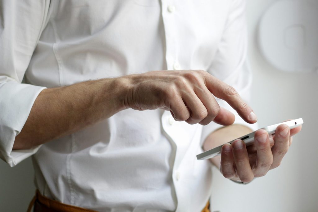 personne tenant un smartphone Android blanc avec une chemise blanche